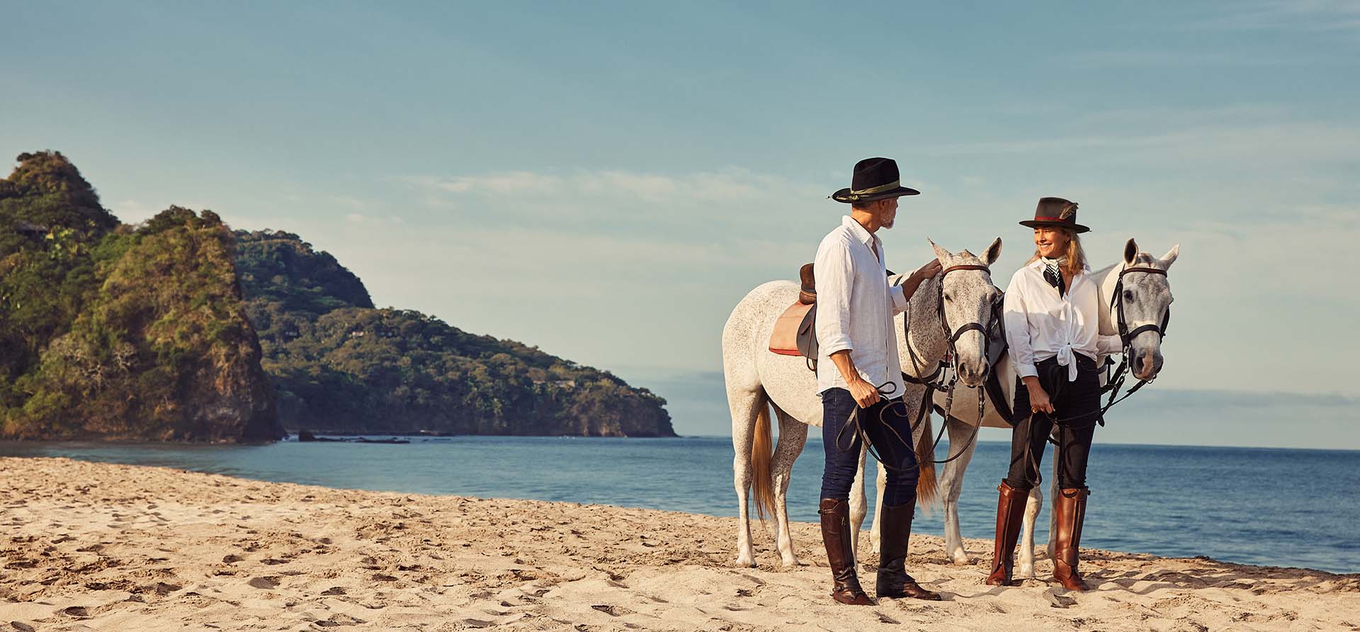 man and woman stand with horses on the beach