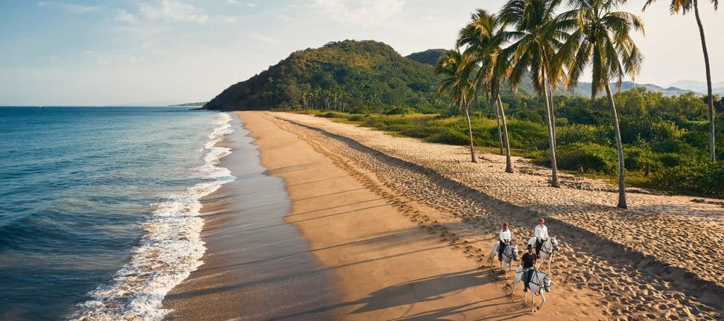 small group rides horses on beaches as sun sets