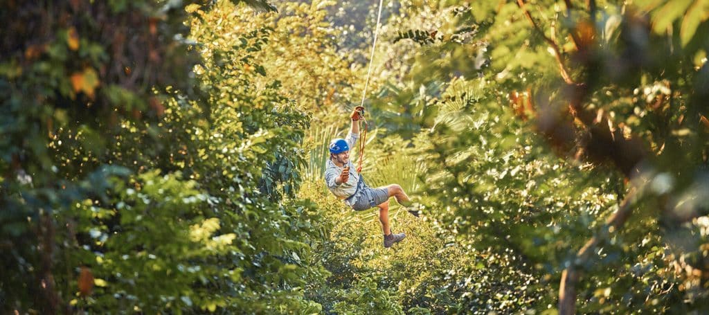 man swings through jungle canopy on zipline
